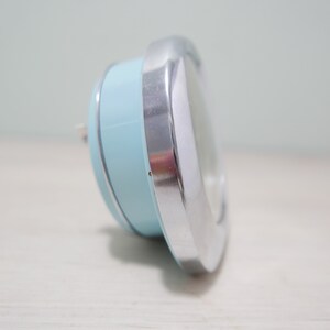 May include: A light blue and silver alarm clock with a round face.
