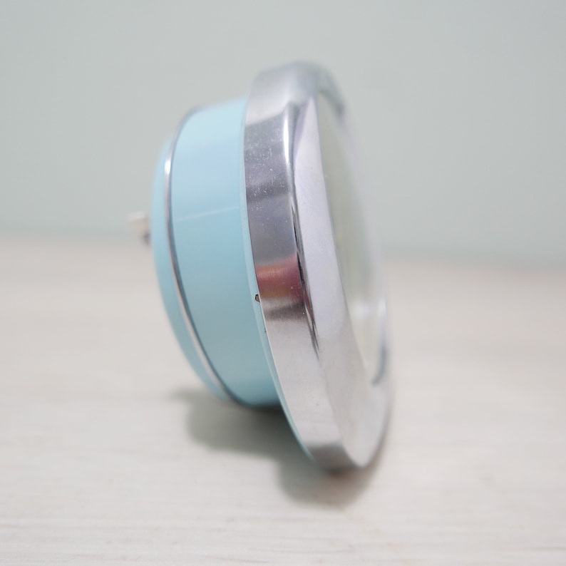 May include: A light blue and silver alarm clock with a round face.