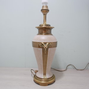 May include: A vintage table lamp with a cream-colored speckled ceramic base and brass accents. The lamp features a decorative brass design and a bulb at the top. The lamp is approximately 24 inches tall.
