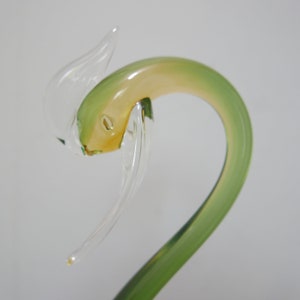 May include: A glass swan figurine with a green and yellow body and clear wings. The swan's head is tilted back and its beak is open.