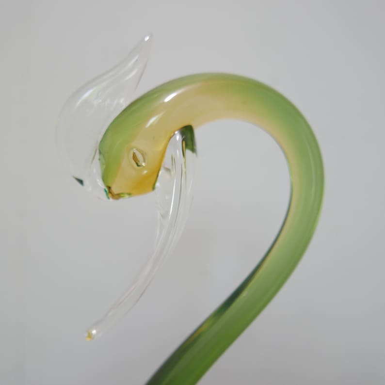 May include: A glass swan figurine with a green and yellow body and clear wings. The swan's head is tilted back and its beak is open.