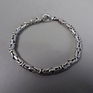 Puede incluir: Un brazalete de cadena de plata con cierre de caja.