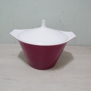 May include: A maroon and white serving bowl with a lid. The bowl has a flared shape and a white lid with a small handle. The handles on the bowl are white. The bowl is sitting on a light-coloured wooden surface.
