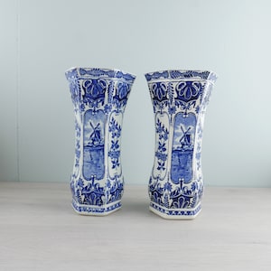 Op de afbeelding: Twee blauwe en witte keramische vazen met een windmolenontwerp. De vazen zijn achthoekig en hebben een traditionele Nederlandse Delftware-stijl.