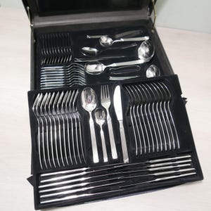 May include: A black leather case with a silver cutlery set inside. The case is open and the cutlery is arranged in rows. The cutlery includes forks, knives, spoons, and serving utensils.