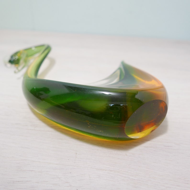 May include: A green and amber glass sculpture in the shape of a swan with a long neck.