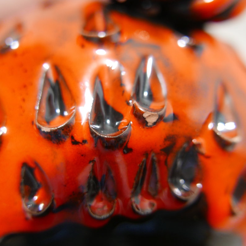 May include: Close-up of a ceramic object with a textured surface. The object is orange with black accents and has a glossy finish.