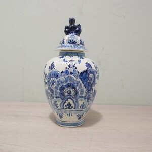 May include: A blue and white ceramic jar with a floral design and a lid with a small knob on top.