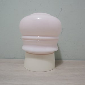 May include: A white lampshade with a pink glass top and a white base. The lampshade has a rounded top and a slightly flared bottom.