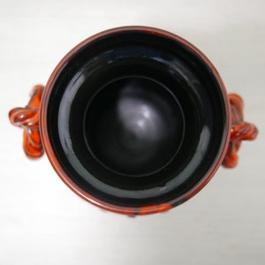 May include: A black and orange ceramic vase with a wide opening and two handles shaped like stylized animal heads.
