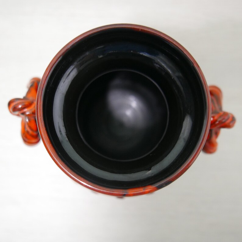 May include: A black and orange ceramic vase with a wide opening and two handles shaped like stylized animal heads.