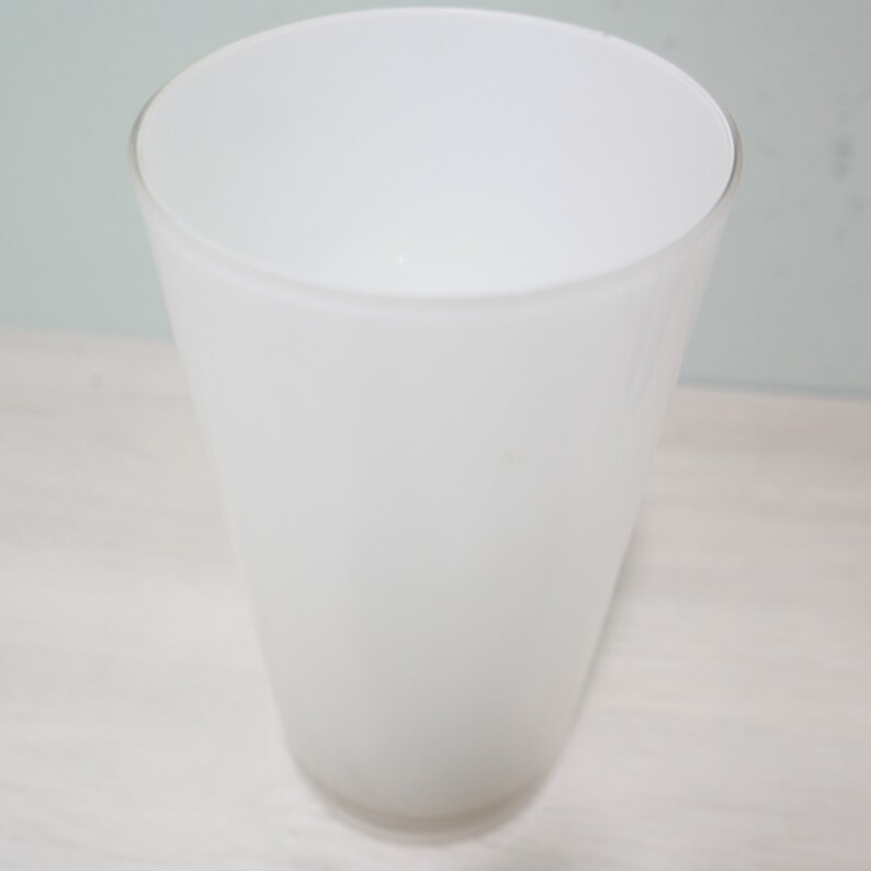 K&ouml;nnte beinhalten: Eine wei&szlig;e Keramiktasse mit einer glatten, abgerundeten Form. Die Tasse ist leer und scheint aus einem dicken, strapazierf&auml;higen Material hergestellt zu sein.