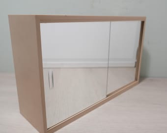 May include: A light-colored wooden cabinet with two sliding mirrored doors. The cabinet has a rectangular shape and is designed to be mounted on a wall. The mirrored doors reflect the surrounding environment.