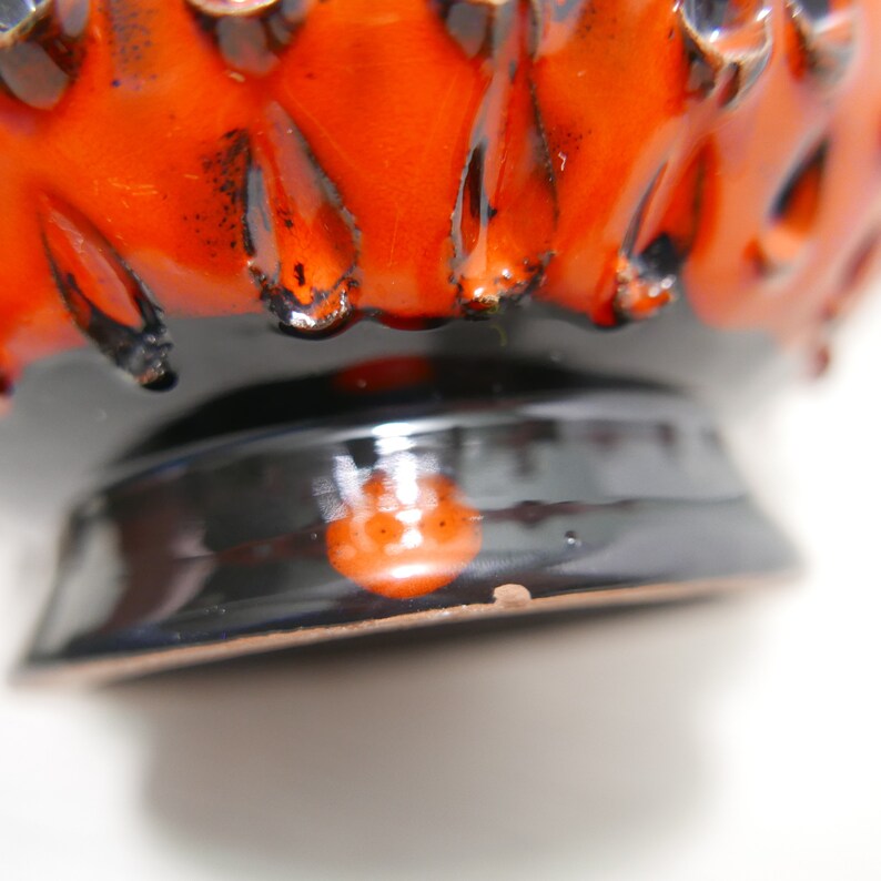May include: A black and orange ceramic vase with a textured, spiky design. The vase has a wide, round base.
