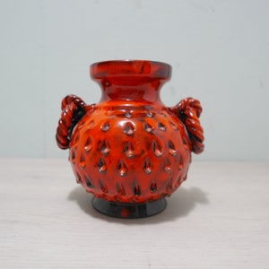 May include: A small, orange ceramic vase with two rope handles. The vase has a textured surface with small, raised dots.