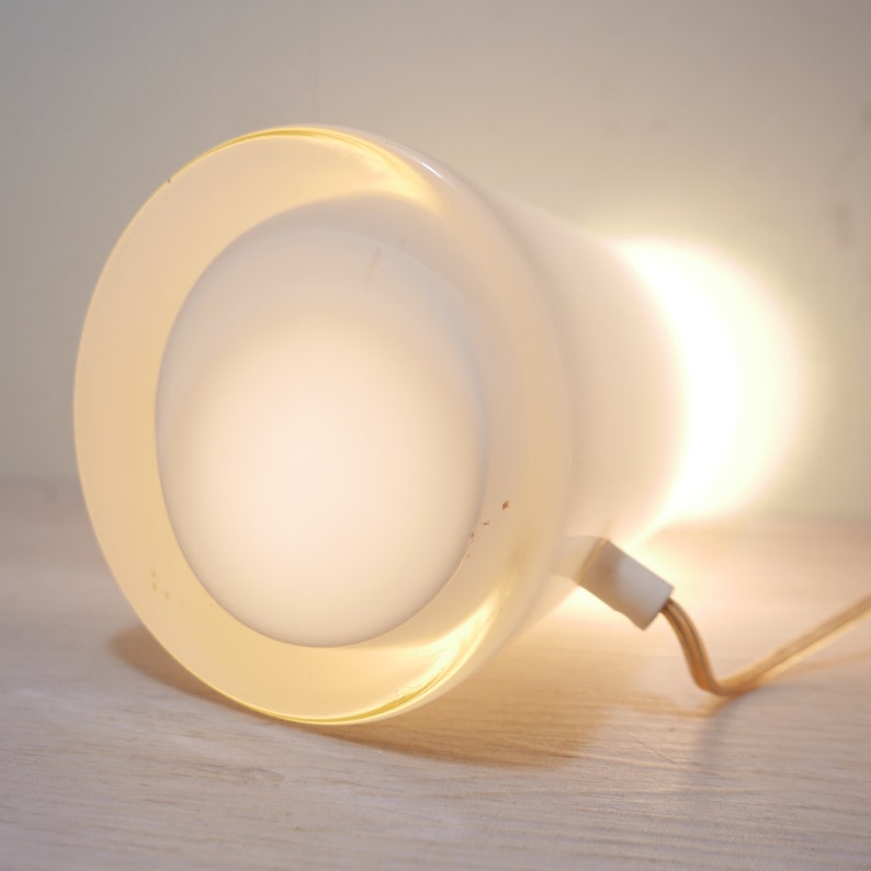 K&ouml;nnte beinhalten: Eine wei&szlig;e Tischlampe mit einem runden, mattierten Glasschirm. Die Lampe hat ein Kabel und einen wei&szlig;en Stecker.