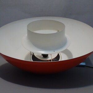 May include: A red and white pendant light fixture with a circular, saucer-shaped shade. The top shade is white and the bottom shade is red.