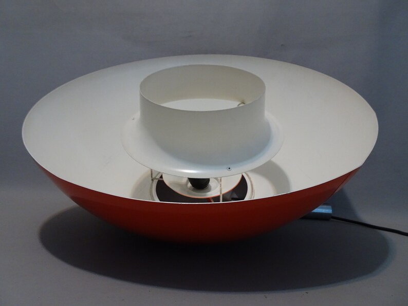 May include: A red and white pendant light fixture with a circular, saucer-shaped shade. The top shade is white and the bottom shade is red.