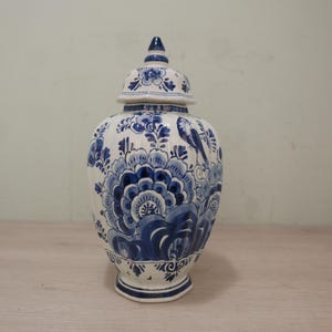 Op de afbeelding: Een wit en blauw keramieken gemberpot met een deksel. De pot is versierd met een bloemen- en vogelontwerp in blauwtinten. De pot heeft een bolvorm en een voetstuk. Het deksel heeft een kleine knop.