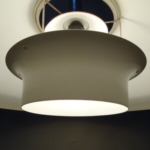 May include: A white ceiling light fixture with a round, white shade. The light is on and illuminating the room.
