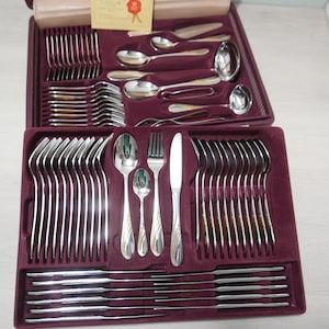 Könnte beinhalten: Ein Set silbernes Besteck in einem burgunderfarbenen Samt-Etui. Das Besteck umfasst Gabeln, Messer, Löffel und Servierstücke.