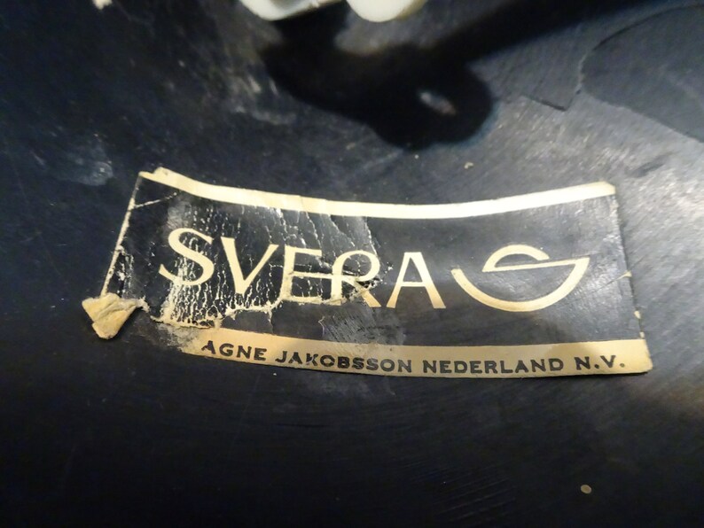May include: A close-up of a black label with gold lettering that reads "SVERA AGNE JAKOBSSON NEDERLAND N.V."