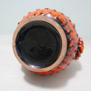 May include: Orange and black ceramic vase with a textured surface and a round base. The vase has a unique design with raised bumps and a textured pattern.