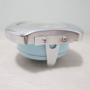 May include: A light blue metal alarm clock with a silver metal frame and two screws on the side.
