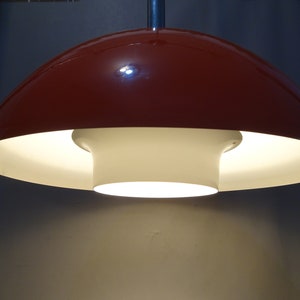 May include: A red and white ceiling lamp with a mushroom-shaped shade. The lamp is turned on and the light is shining through the white shade.