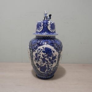 May include: A blue and white ceramic jar with a lid featuring a floral design. The lid is topped with a small blue and white ceramic figurine of a dog.