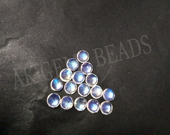 May include: A group of 16 iridescent moonstone cabochons, each with a round shape and a smooth, polished surface. The stones are arranged in a triangular pattern on a black background.