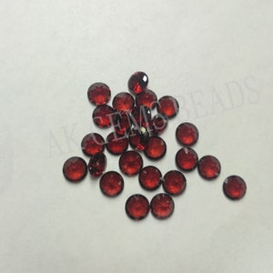 May include: A group of 25 round, red gemstones. The gemstones are scattered on a white surface.