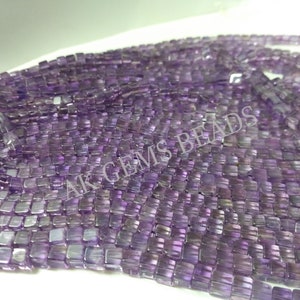 Puede incluir: Primer plano de una colección de cuentas cuadradas de color amatista. Las cuentas están ensartadas, creando una apariencia fluida y texturizada. La imagen está bien iluminada, resaltando la calidad translúcida de las cuentas. El texto "AK GEMS BEADS" es visible.