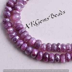 Puede incluir: Una hebra de cuentas de piedras preciosas facetadas de color púrpura. Las cuentas son redondas y tienen un acabado brillante y pulido. Las cuentas están enhebradas en un hilo transparente. La imagen está etiquetada como "AKGems Beads".