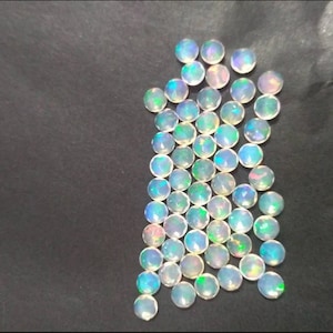 May include: A collection of 40 round, white opal cabochons with iridescent rainbow flashes. The stones are approximately 6mm in diameter and have a smooth, polished finish.