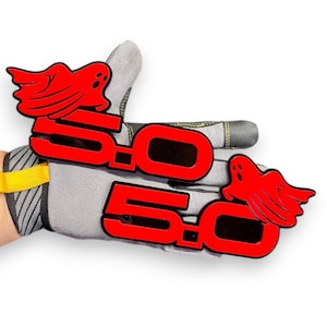 Puede incluir: Dos emblemas de fantasma 5.0 rojos se muestran en guantes de trabajo grises. Los emblemas presentan el número 5.0 en negrita, con un diseño de fantasma rojo encima de cada número. Los guantes tienen una correa de muñeca amarilla.