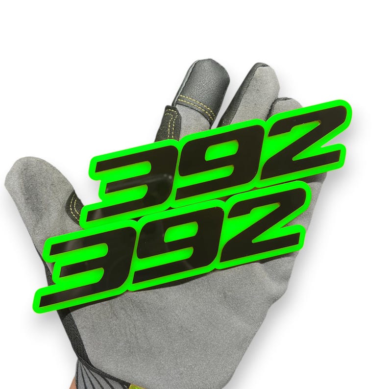 May include: Two black and green "392" decals are displayed on a grey work glove. The decals have a neon green outline and are angled across the glove. The glove is made of grey suede-like material.