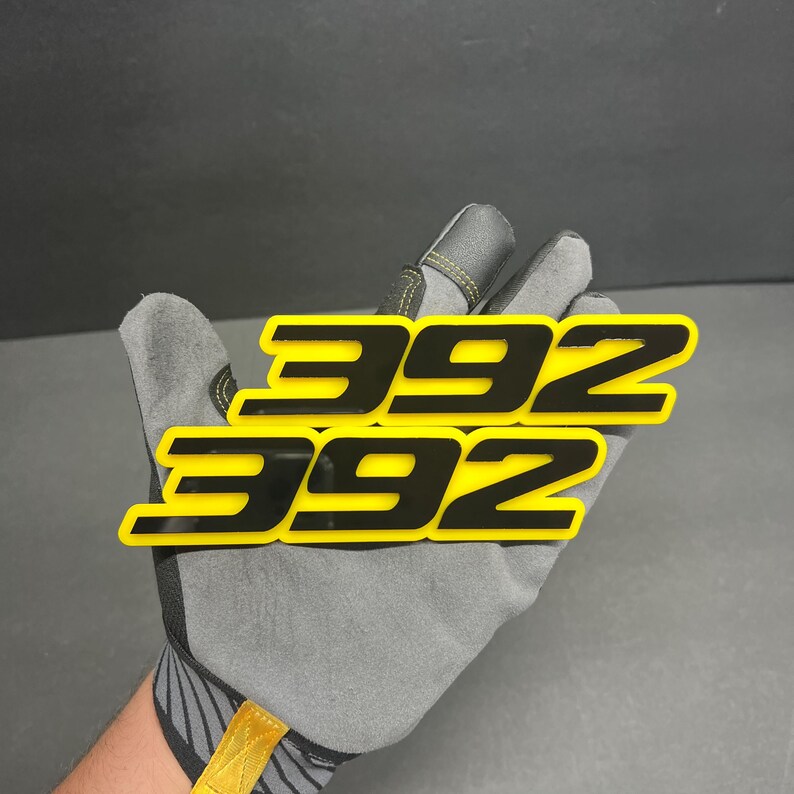 May include: A set of three cream-glazed ceramic mugs with a speckled finish. Each mug is hand-painted with a different design: a blue and green leaf, a yellow flower, and a red berry. The mugs have a simple, modern design.