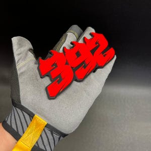 May include: A red and black graphic of the number "392" in a graffiti style is displayed. The graphic is held by a gray work glove with yellow accents. The background is black.