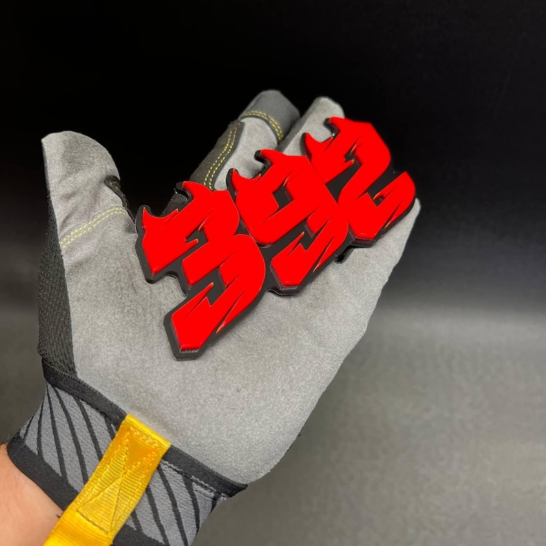 May include: A red and black graphic of the number "392" in a graffiti style is displayed. The graphic is held by a gray work glove with yellow accents. The background is black.