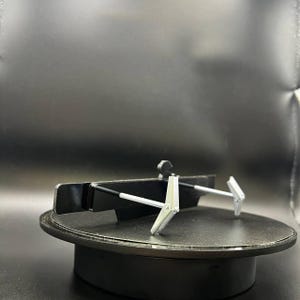 May include: A black and silver metal object with two silver arms extending from a black base. The object is on a black rotating platform. The arms have a hinged design.