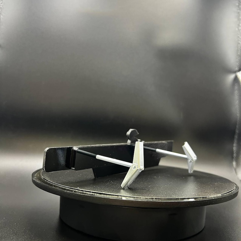 May include: A black and silver metal object with two silver arms extending from a black base. The object is on a black rotating platform. The arms have a hinged design.