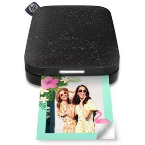 May include: A black and white speckled portable photo printer with the HP logo on top. A color photo is emerging from the printer, featuring two women in floral dresses and sunglasses. The photo has a tropical theme with flowers and a flamingo.