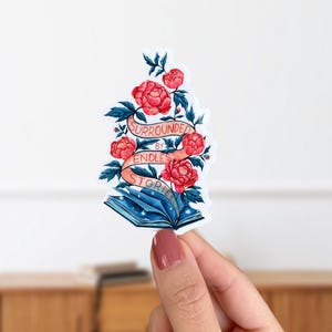 May include: A sticker featuring an open book with blue and white pages and stars. The book is surrounded by pink flowers and a banner that reads "Surrounded by Endless Stories".