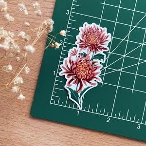 Peut inclure: Un autocollant repr&eacute;sentant un motif floral avec deux chrysanth&egrave;mes roses et des feuilles vertes sur fond blanc.
