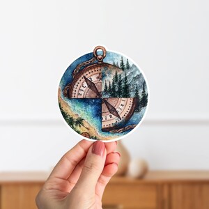 Puede incluir: Una pegatina redonda con un diseño de brújula. La brújula está dividida en cuatro secciones, cada una representando un paisaje diferente: una playa, un bosque, una cordillera y un cielo estrellado. La aguja de la brújula apunta hacia el norte.