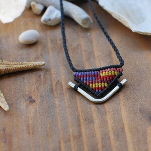 May include: A black cord necklace with a silver triangle pendant. The pendant is woven with colorful threads in red, yellow, and blue.