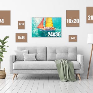 May include: A living room scene featuring a gray sofa, a green blanket, and a floor lamp. Various canvas prints in brown frames are displayed on the wall, including sizes 18x24, 8x10, 11x14, 24x36, 16x20, and 20x20 inches. A sailboat painting is the focal point.