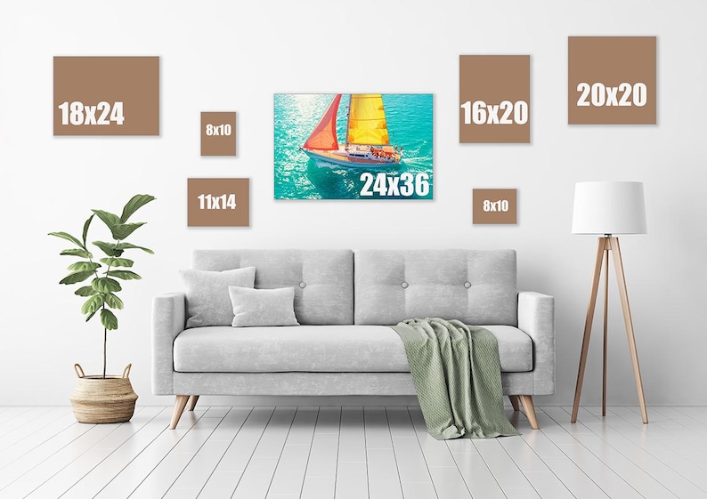 May include: A living room scene featuring a gray sofa, a green blanket, and a floor lamp. Various canvas prints in brown frames are displayed on the wall, including sizes 18x24, 8x10, 11x14, 24x36, 16x20, and 20x20 inches. A sailboat painting is the focal point.