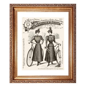 May include: Framed vintage print featuring two women in period clothing posing with bicycles. The print has a sepia tone and includes French text, with the words "ROSFELDER FRERES" prominently displayed. The frame is ornate and gold-colored.